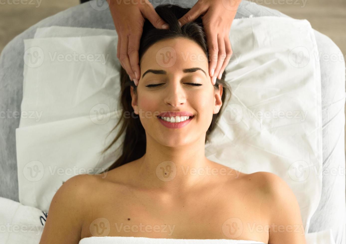 mujer sonriente joven que recibe un masaje de cabeza en un centro de spa. foto