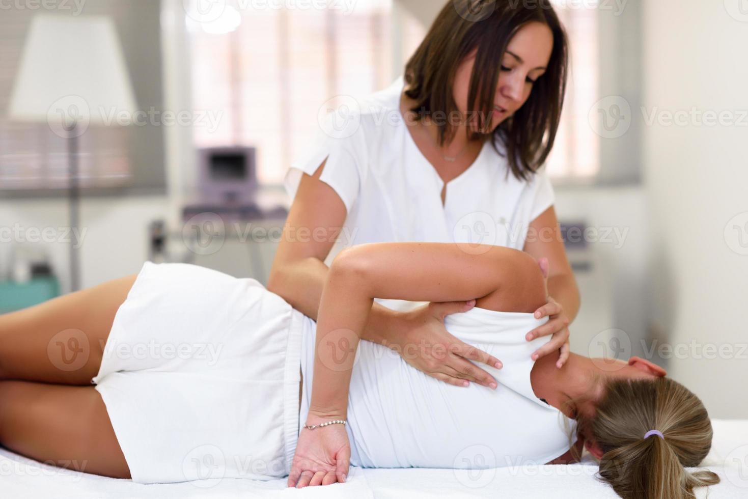 Professional female physiotherapist giving shoulder massage to blonde woman photo