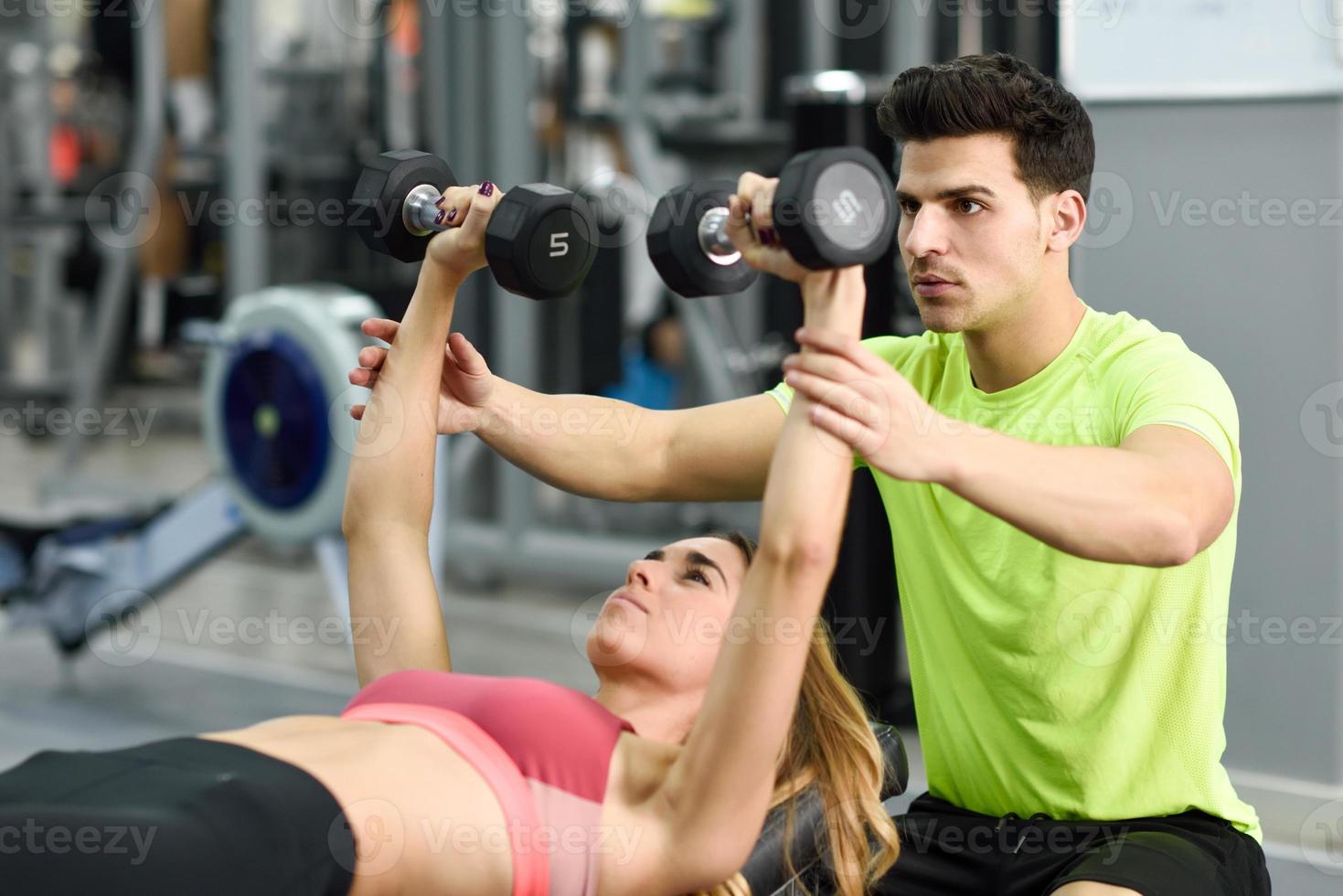 entrenador personal ayudando a una mujer joven a levantar pesas foto