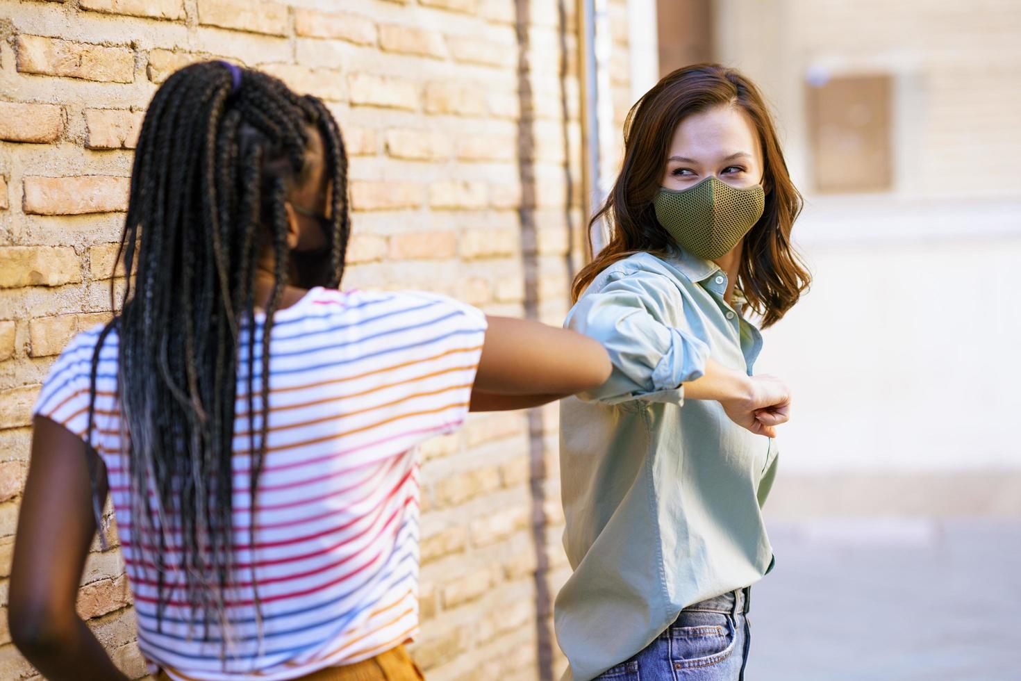 Mujeres jóvenes multiétnicas con máscaras saludándose con los codos foto