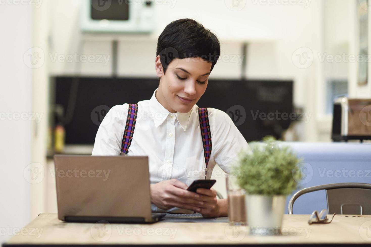 Young businesswoman with very short haircut looking at her smartphone at home. photo