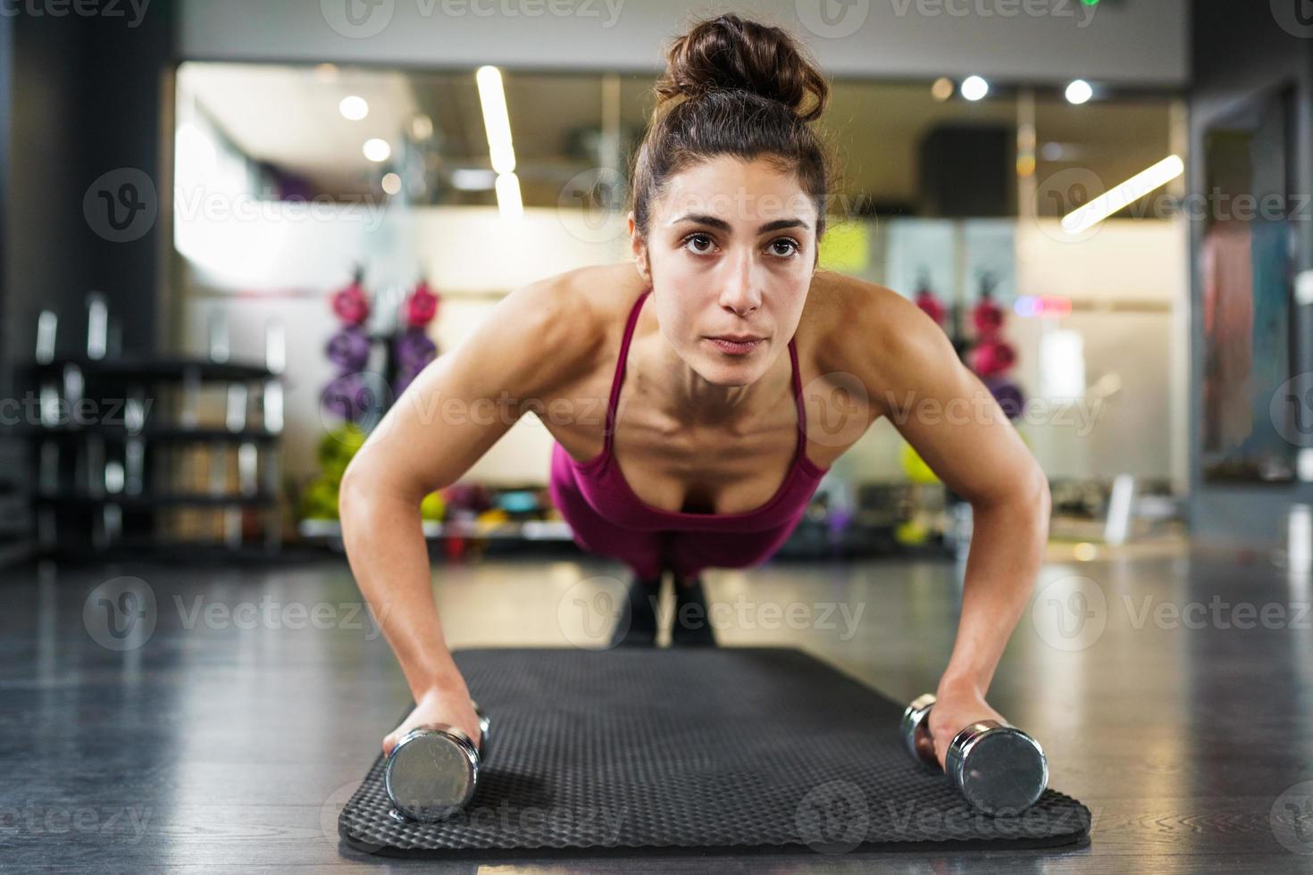 Woman doing push-ups exercise with dumbbell in a fitness workout photo