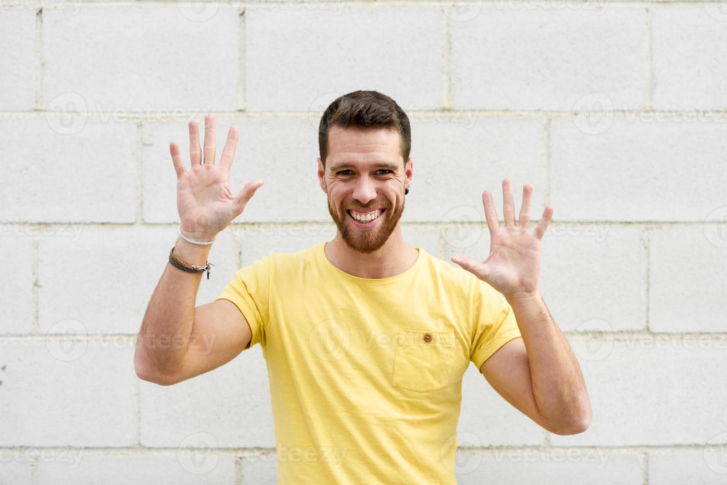 Funny young man on brick wall with open hands smiling. photo