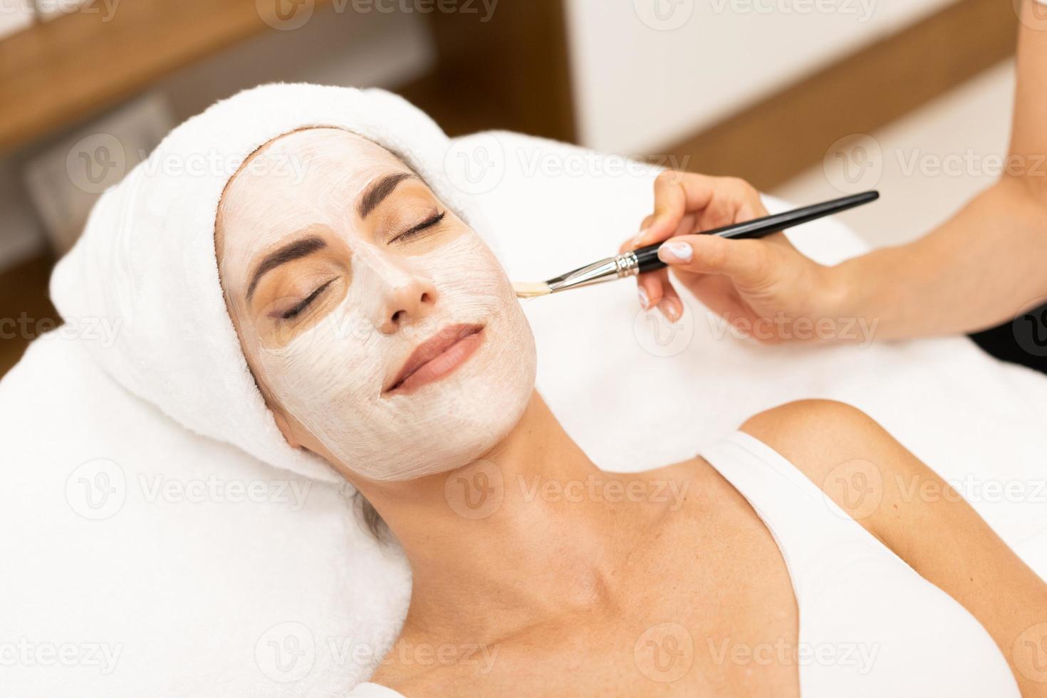 estética aplicando una mascarilla en el rostro de una mujer de mediana edad en un moderno centro de bienestar. foto