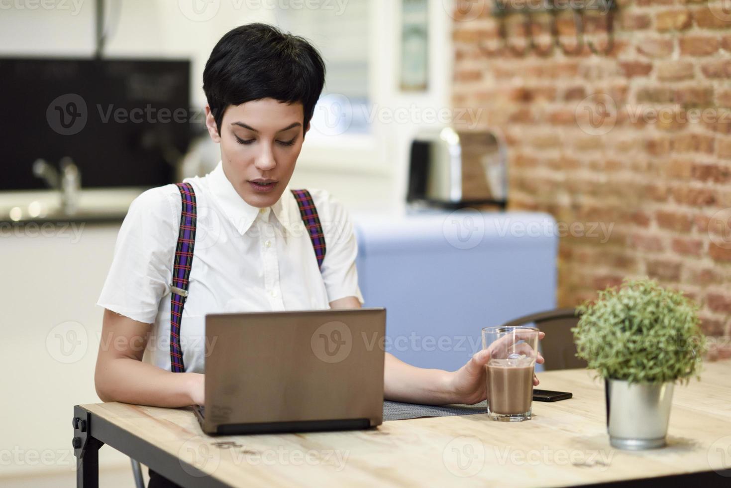 mujer joven con corte de pelo muy corto escribiendo con una computadora portátil en casa. foto