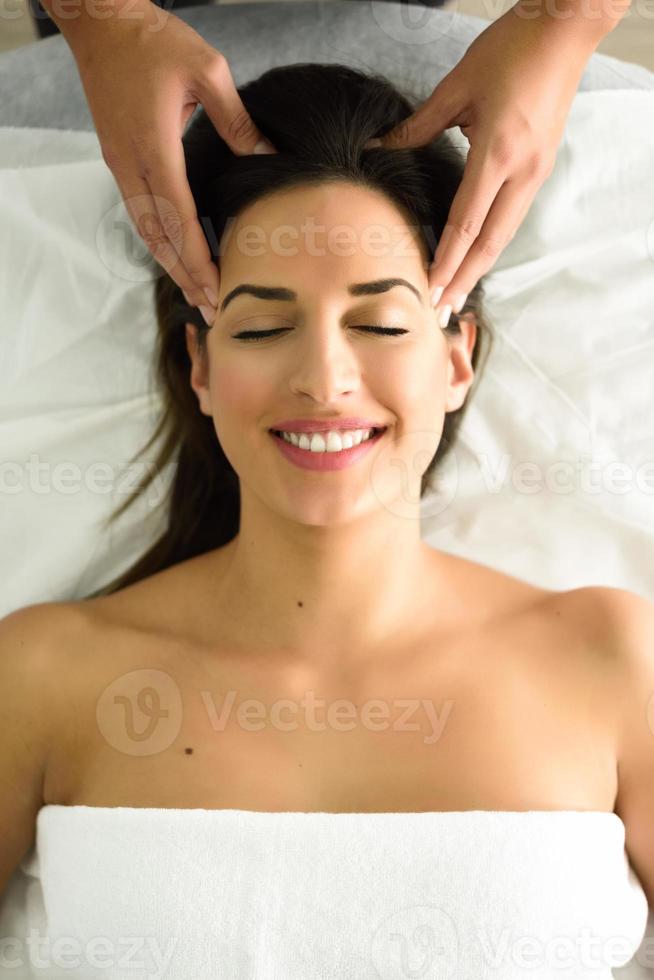 mujer sonriente joven que recibe un masaje de cabeza en un centro de spa. foto