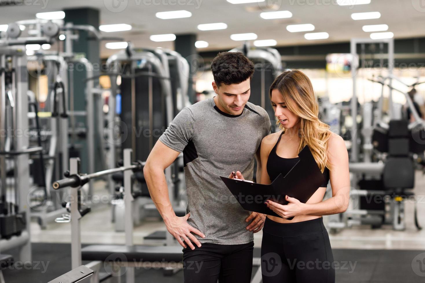 Entrenador personal y cliente mirando su progreso en el gimnasio. foto