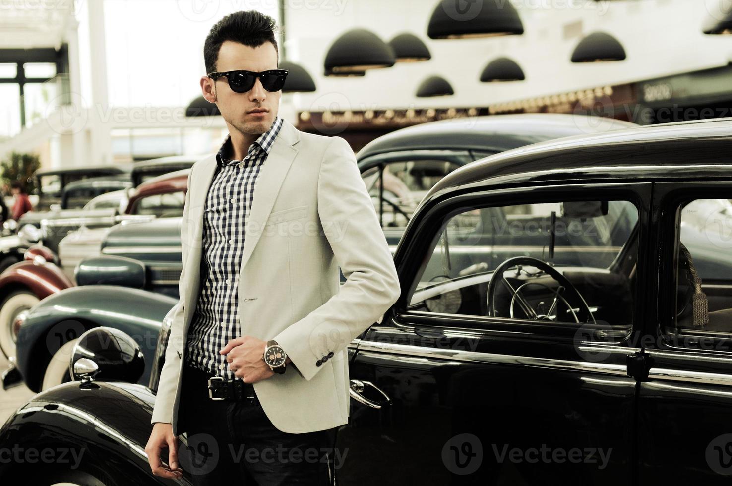 joven apuesto, modelo de moda, vestido con chaqueta y camisa con coches viejos foto