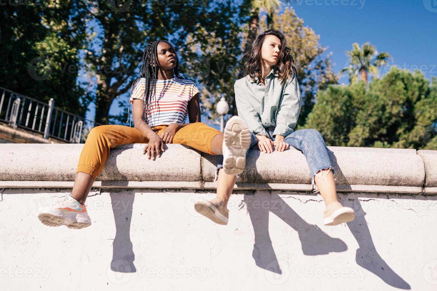 dos mujeres multiétnicas sentadas en una muralla urbana. foto