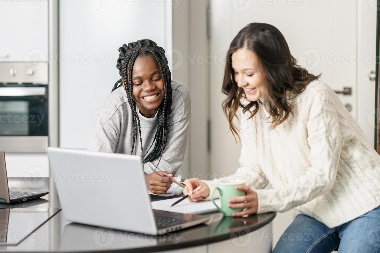 Dos chicas universitarias que estudian juntas en casa con computadoras portátiles mientras beben café foto