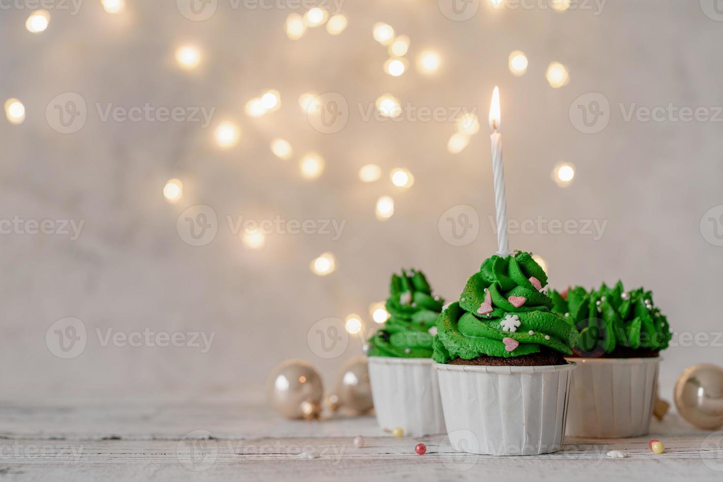 Cupcakes con forma de árbol de Navidad, rodeados de adornos festivos y luces de fondo foto