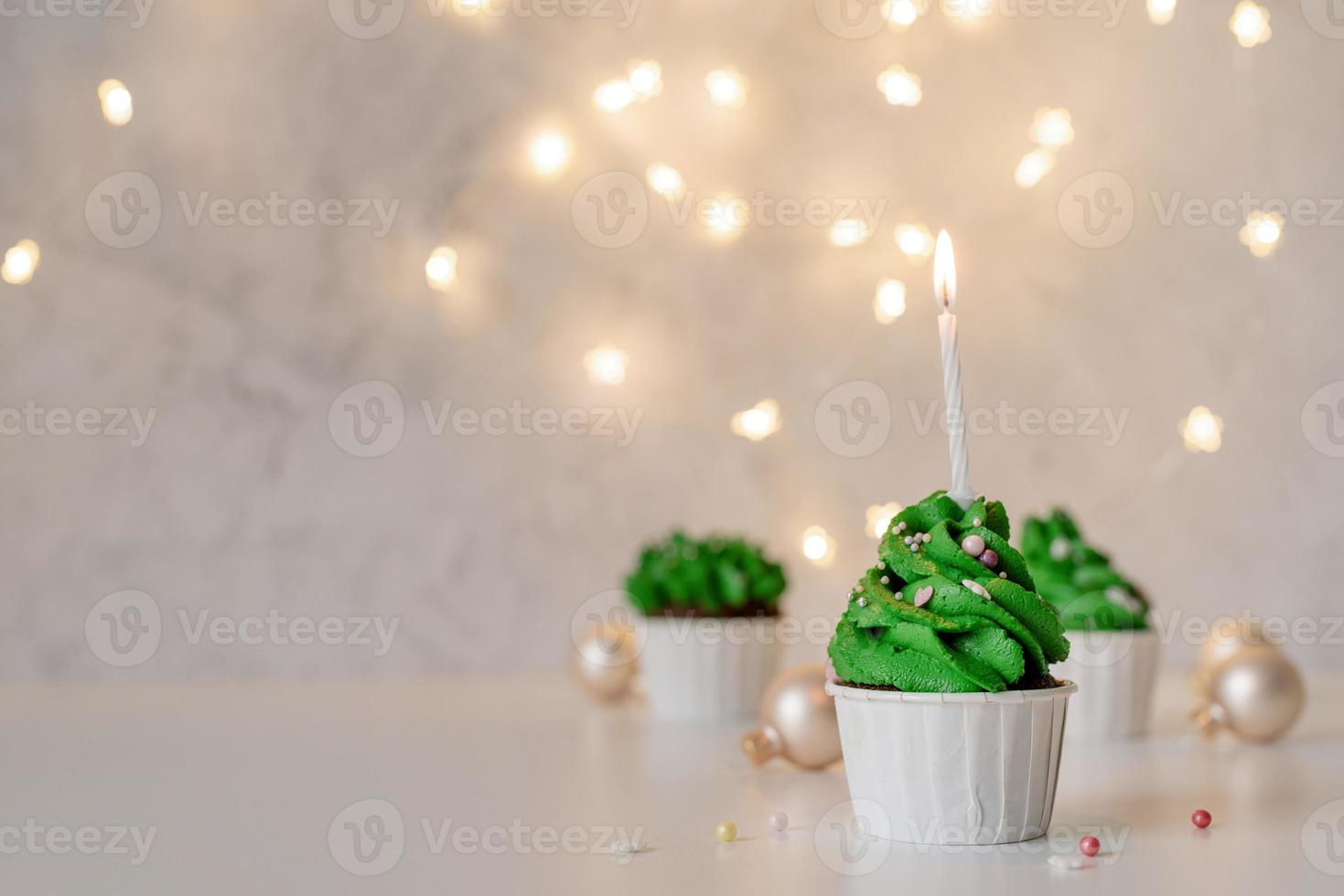 Christmas tree shaped cupcakes, surrounded with festive decorations and lights on the background photo