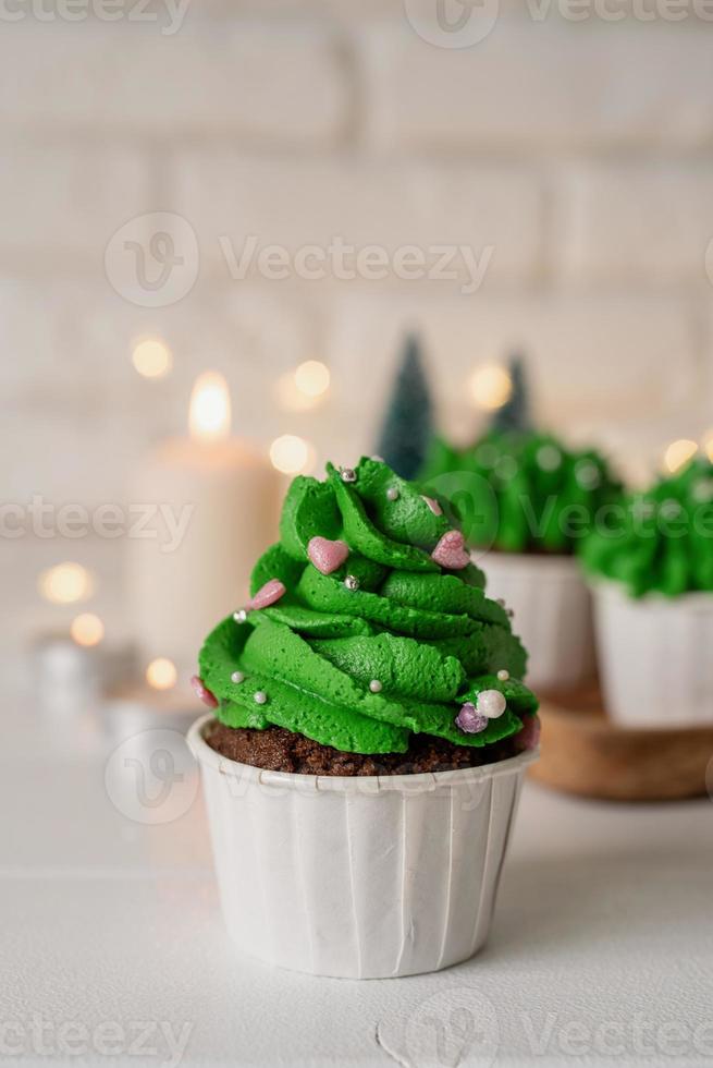 Cupcakes con forma de árbol de Navidad, rodeados de adornos festivos y luces de fondo foto