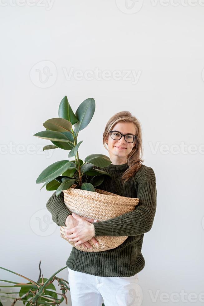 Atractiva mujer joven en un interior amplio y luminoso sosteniendo una planta de ficus foto