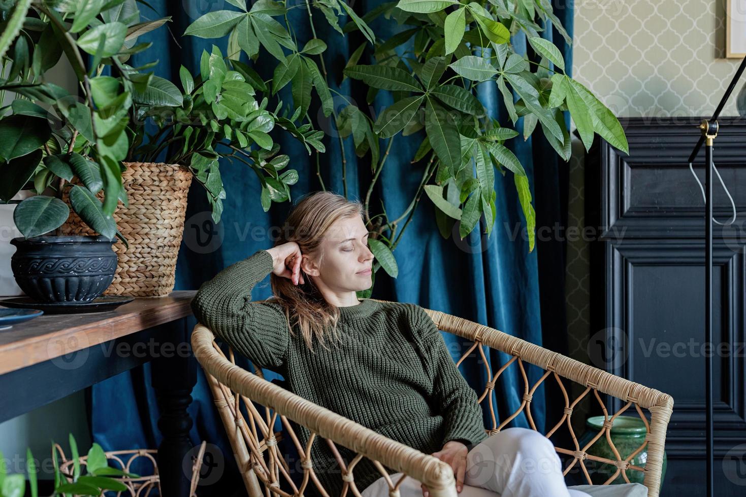 Joven mujer rubia sentada en una silla cómoda rodeada de plantas foto