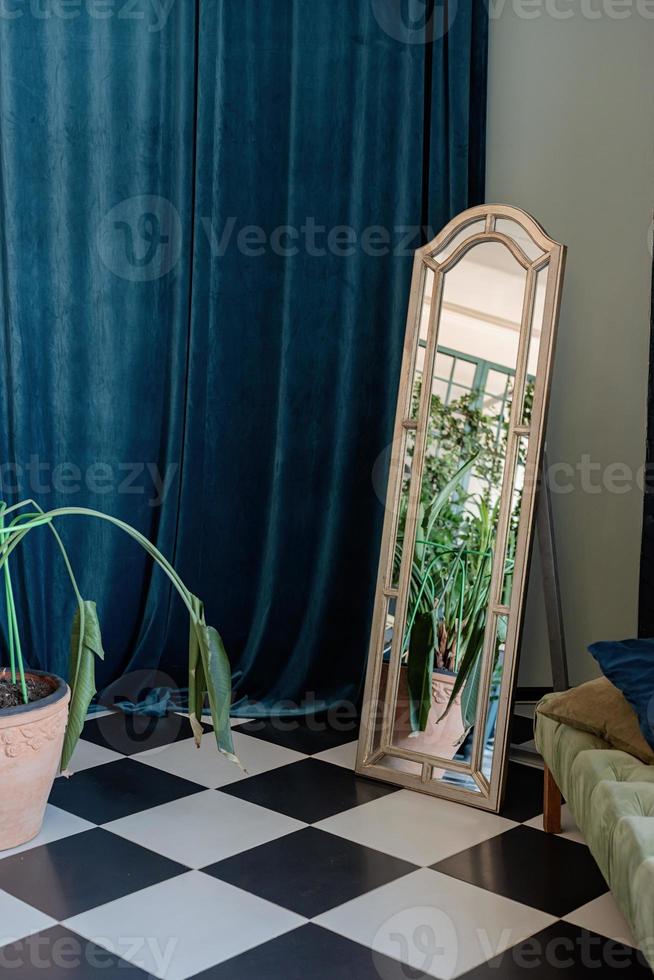 Salón interior de esquina con espejo, cortina azul y plantas. foto