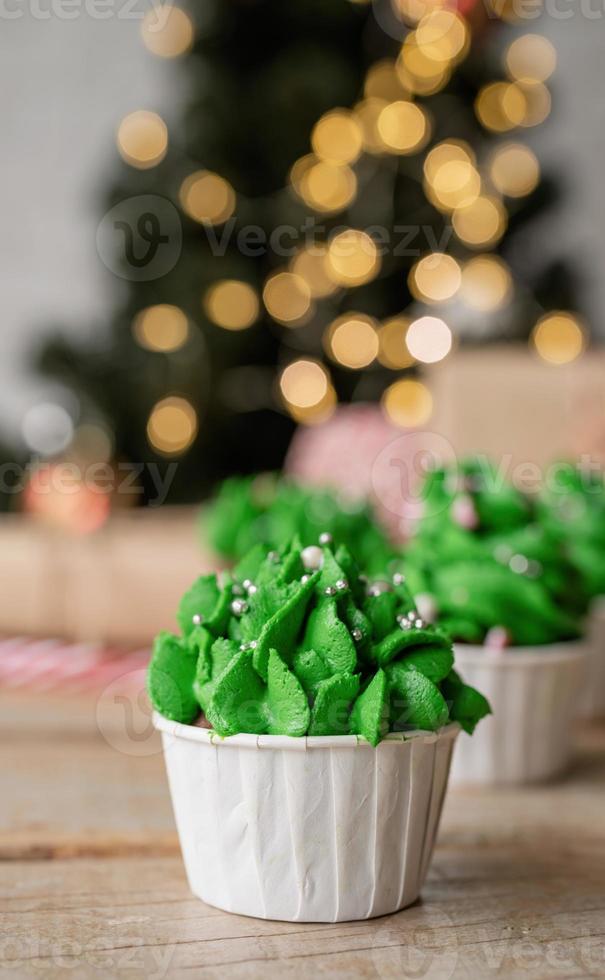 Christmas tree shaped cupcakes, surrounded with festive decorations and lights on the background photo