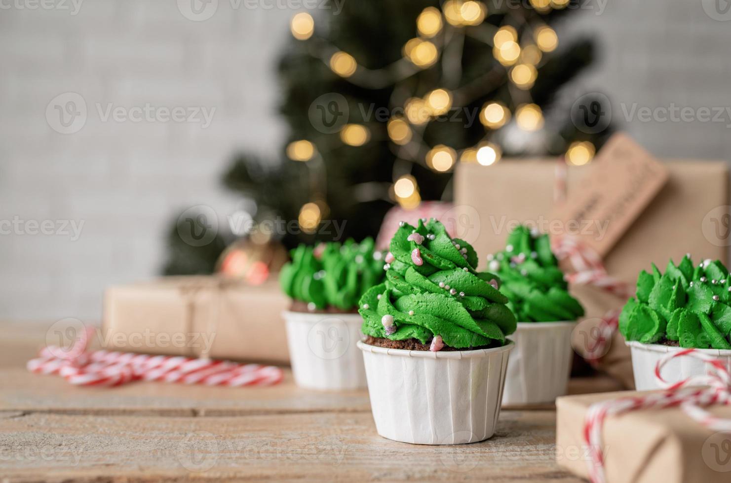 Christmas tree shaped cupcakes, surrounded with festive decorations and lights on the background photo