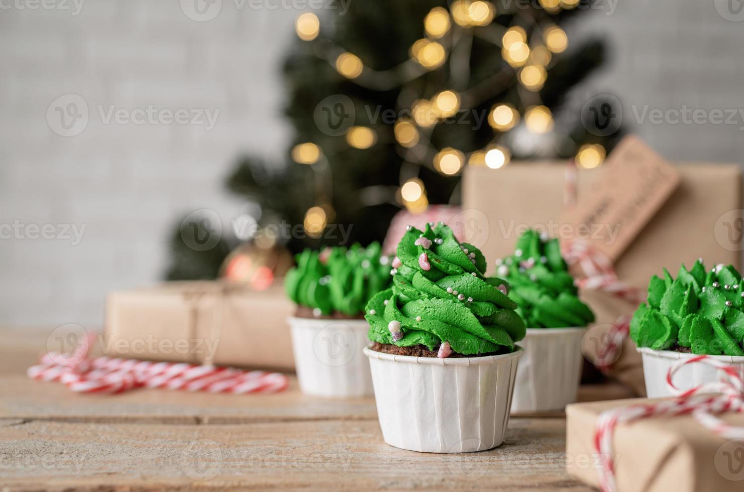 Cupcakes con forma de árbol de Navidad, rodeados de adornos festivos y luces de fondo foto