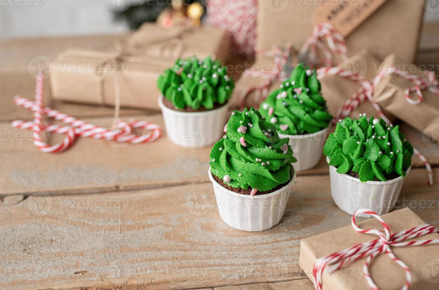 Cupcakes con forma de árbol de Navidad, rodeados de adornos festivos y luces de fondo foto