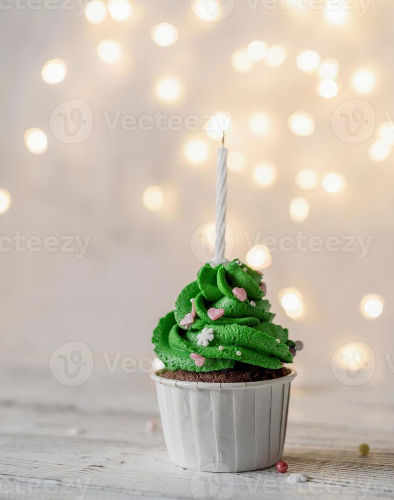 Christmas tree shaped cupcakes, surrounded with festive decorations and lights on the background photo