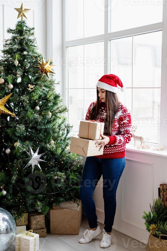 Mujer joven en suéter rojo sosteniendo una pila de regalos de Navidad foto