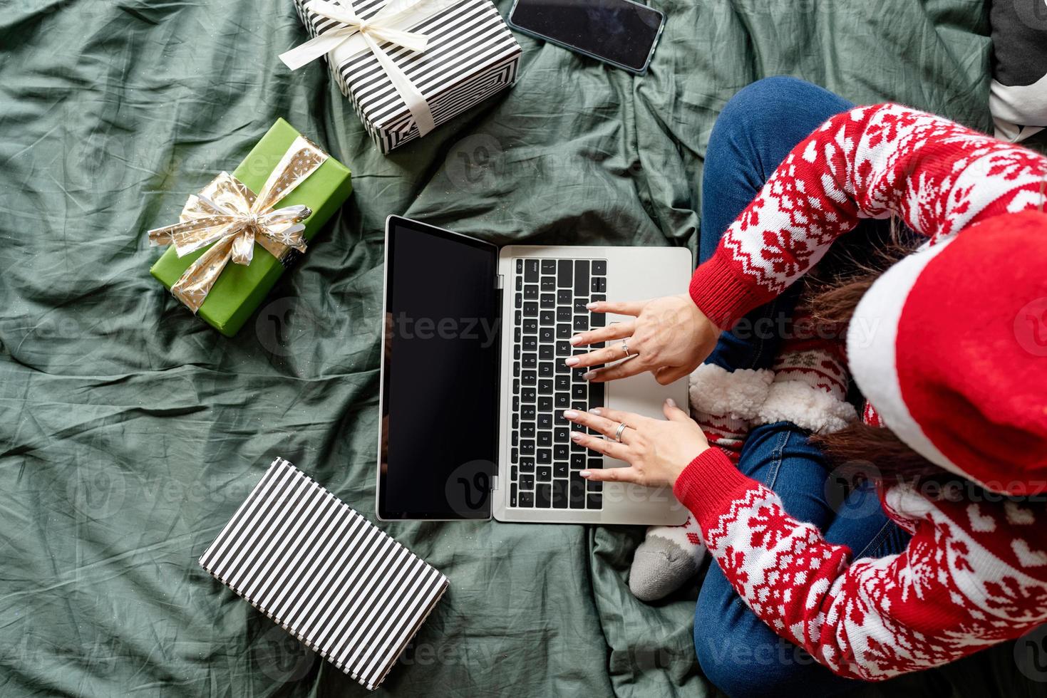 Mujer vistiendo ropa de navidad sentada en la cama usando laptop foto