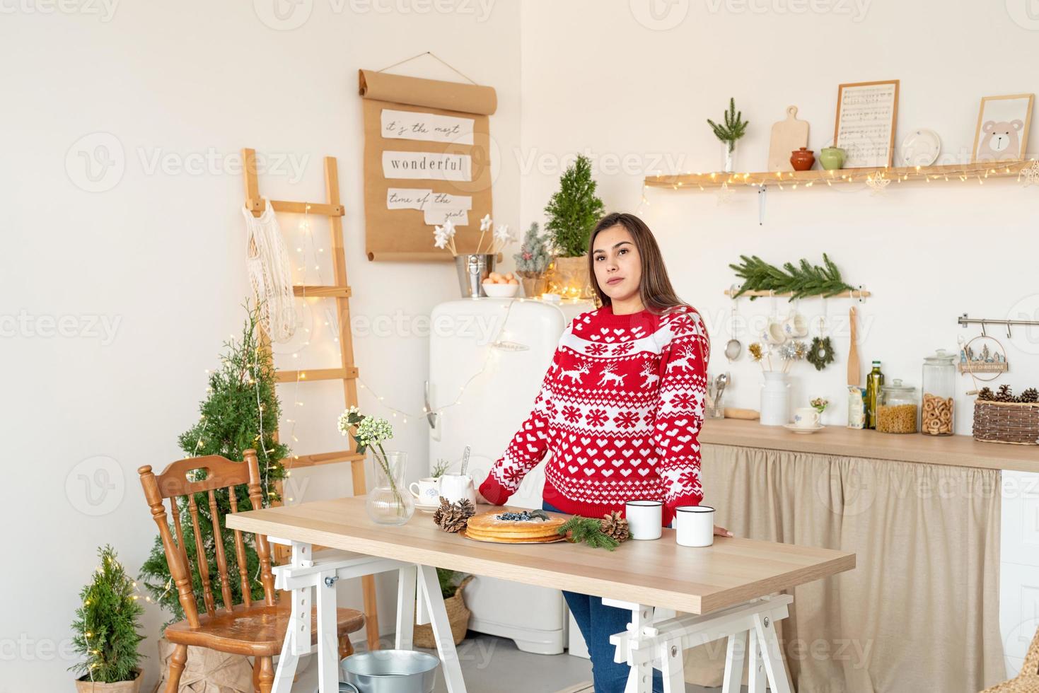 Happy young woman in christmas sweater making hot drinks in the kitchen photo