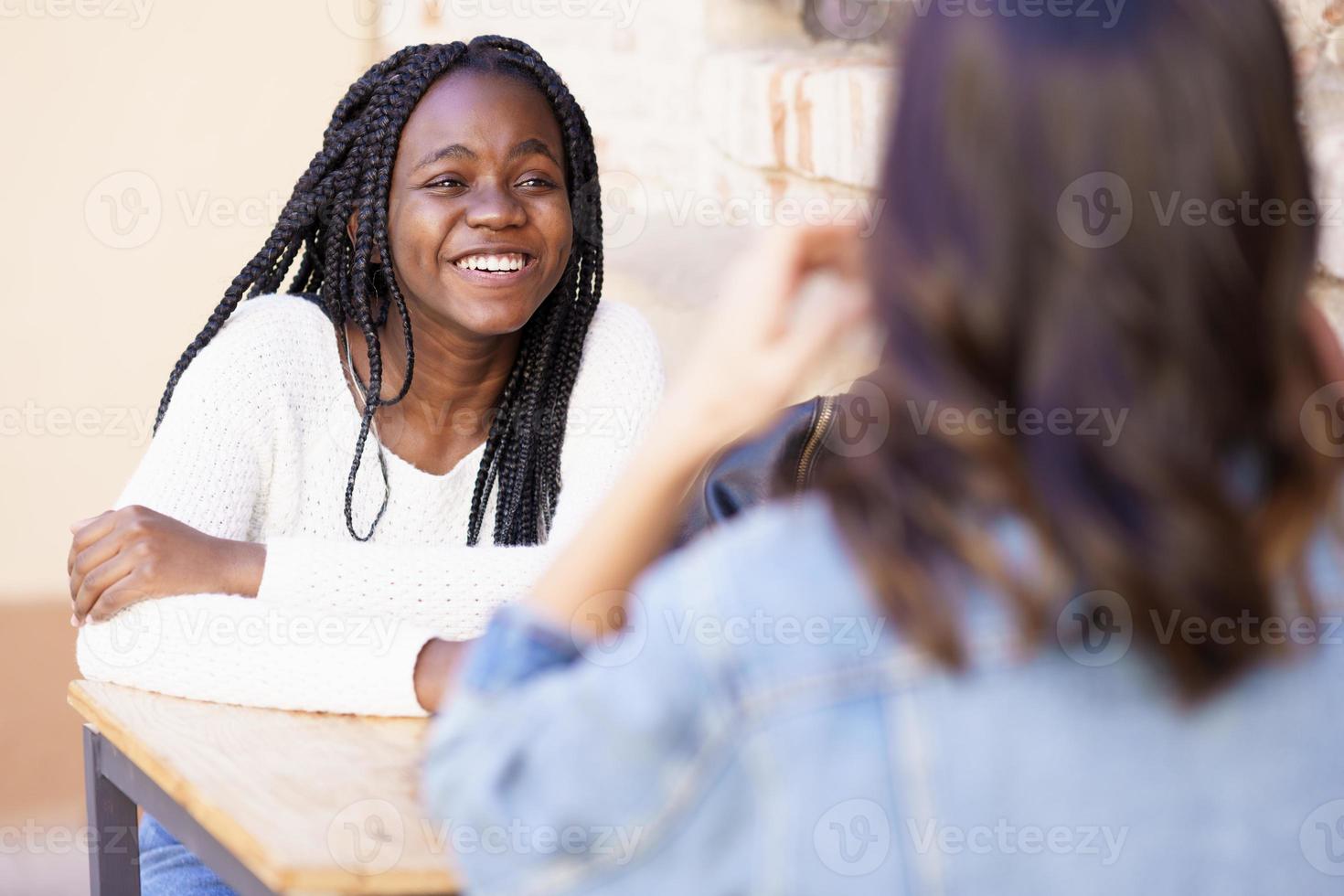 Two multiethnic friends talking sitting at a table outside a bar. photo