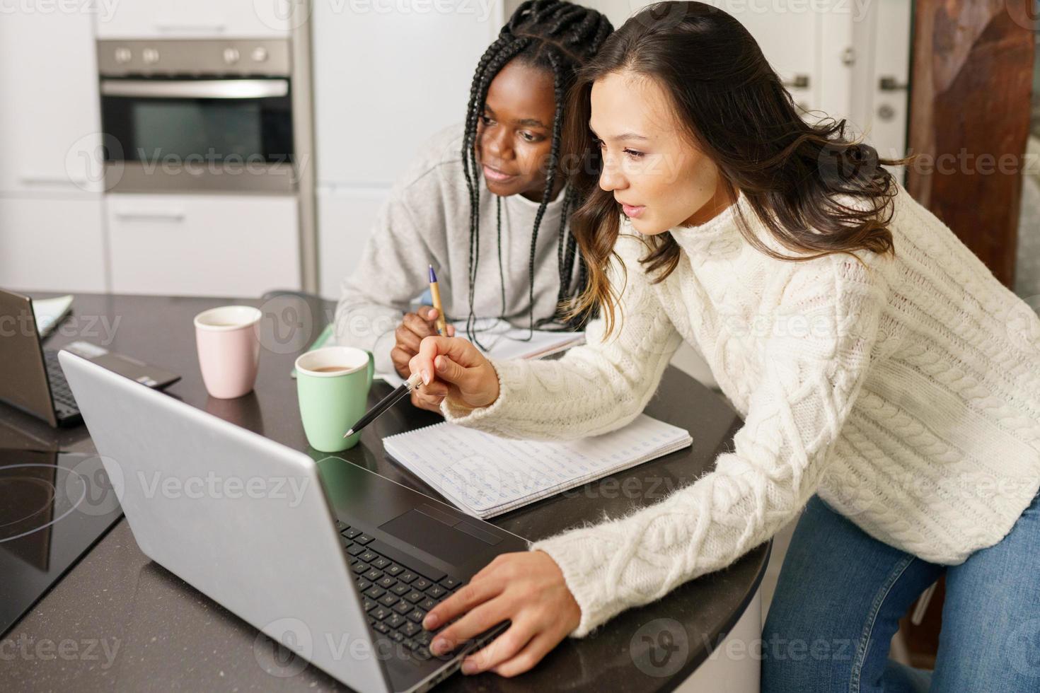 Dos chicas universitarias que estudian juntas en casa con computadoras portátiles mientras beben café foto