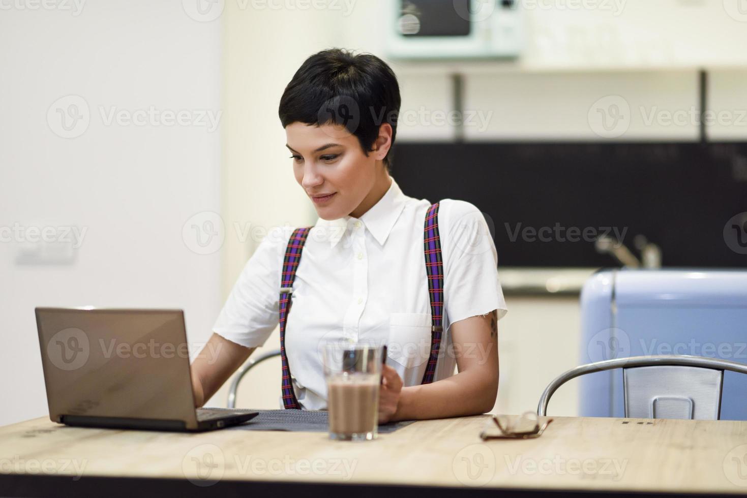 mujer joven con corte de pelo muy corto escribiendo con una computadora portátil en casa. foto