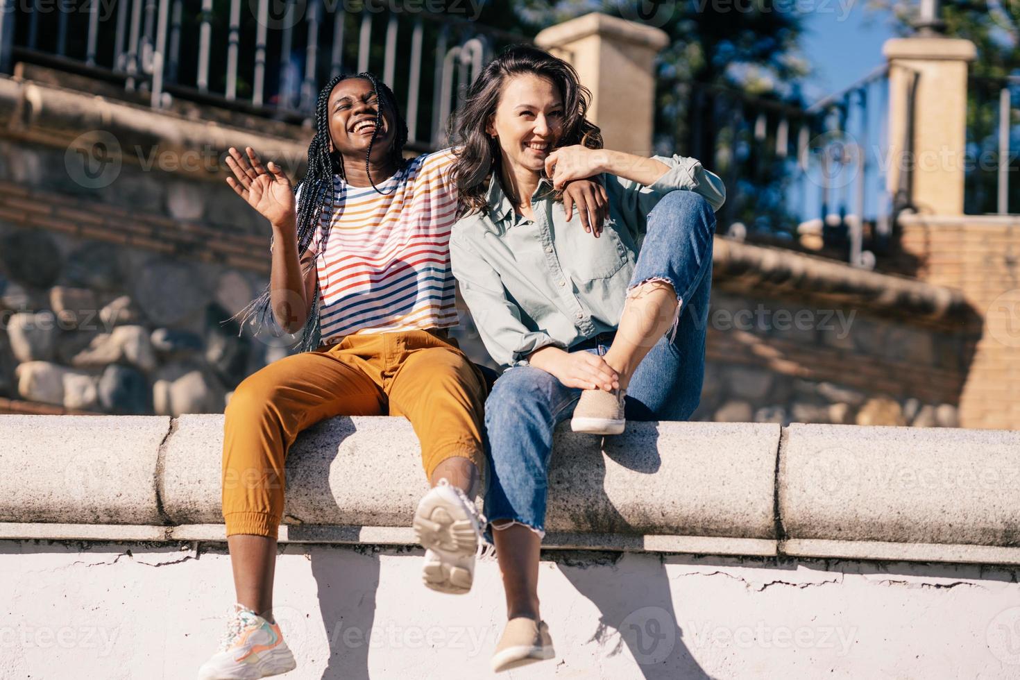 Two friends having fun together on the street sitting on a urban wall. photo