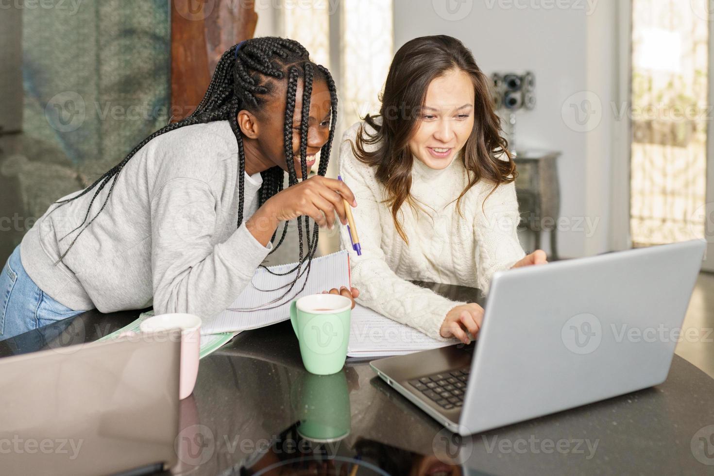 Two college girls studying together at home with laptops while drinking coffee photo