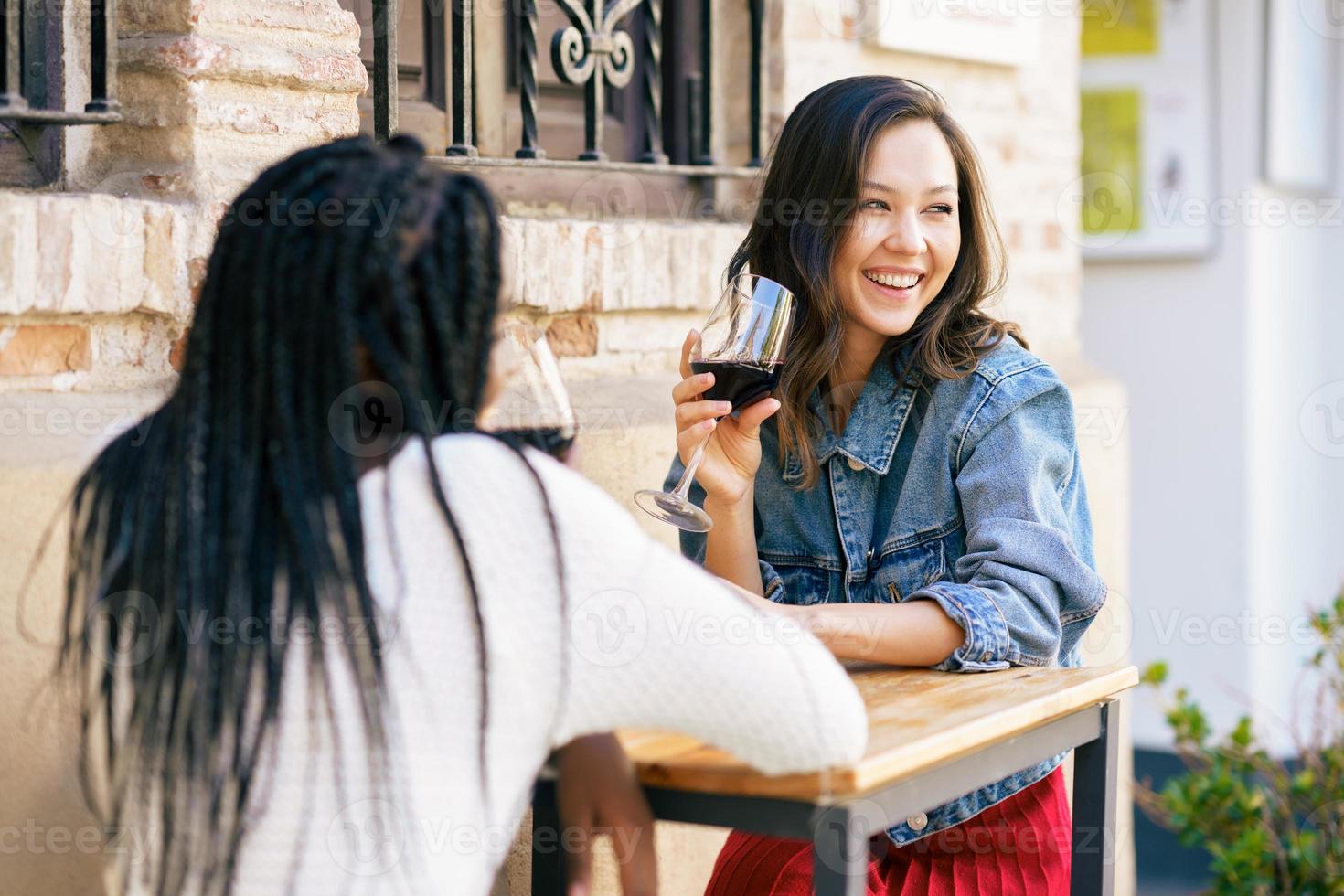 Two women drinking red wine sitting at a table outside a bar. photo