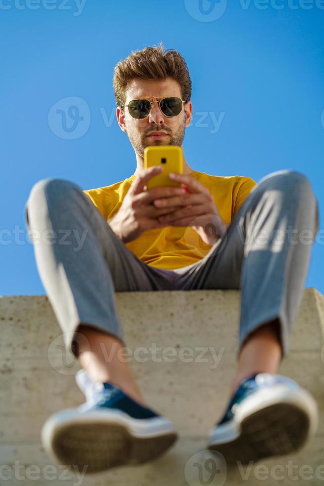 joven con su teléfono inteligente sentado en una repisa exterior foto