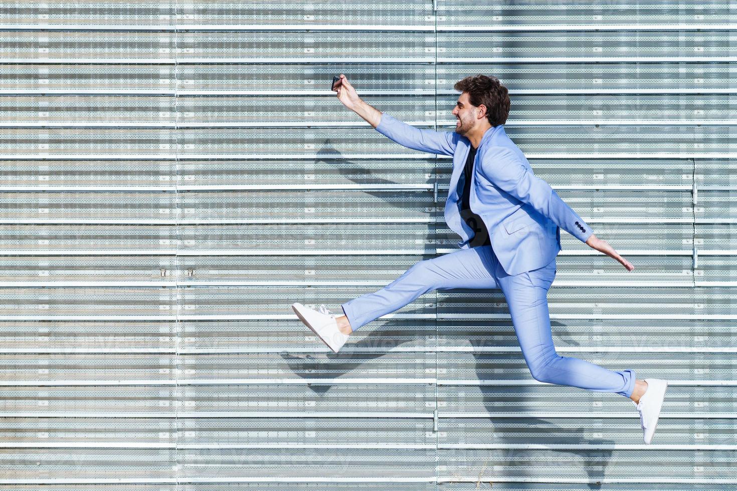 Hombre vestido con traje hace un selfie con un teléfono inteligente mientras salta foto