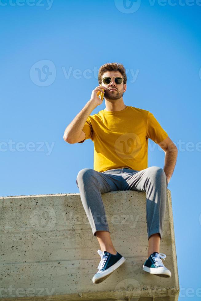 joven con su teléfono inteligente sentado en una repisa exterior foto