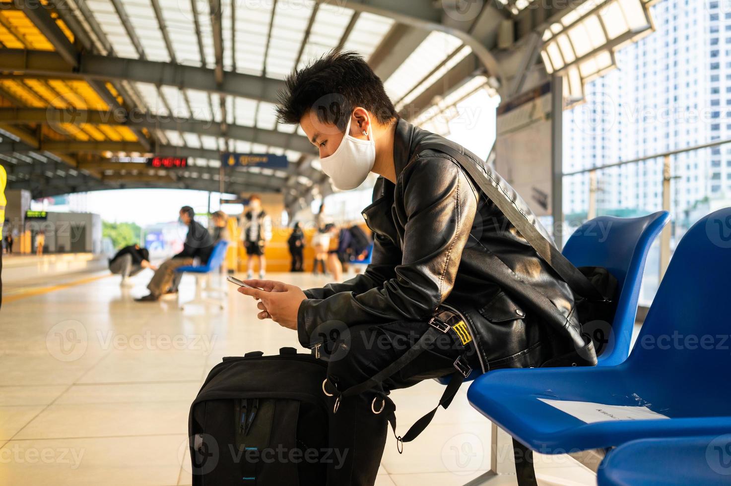 image of asian man sitting and using mobile phone at train station platform photo