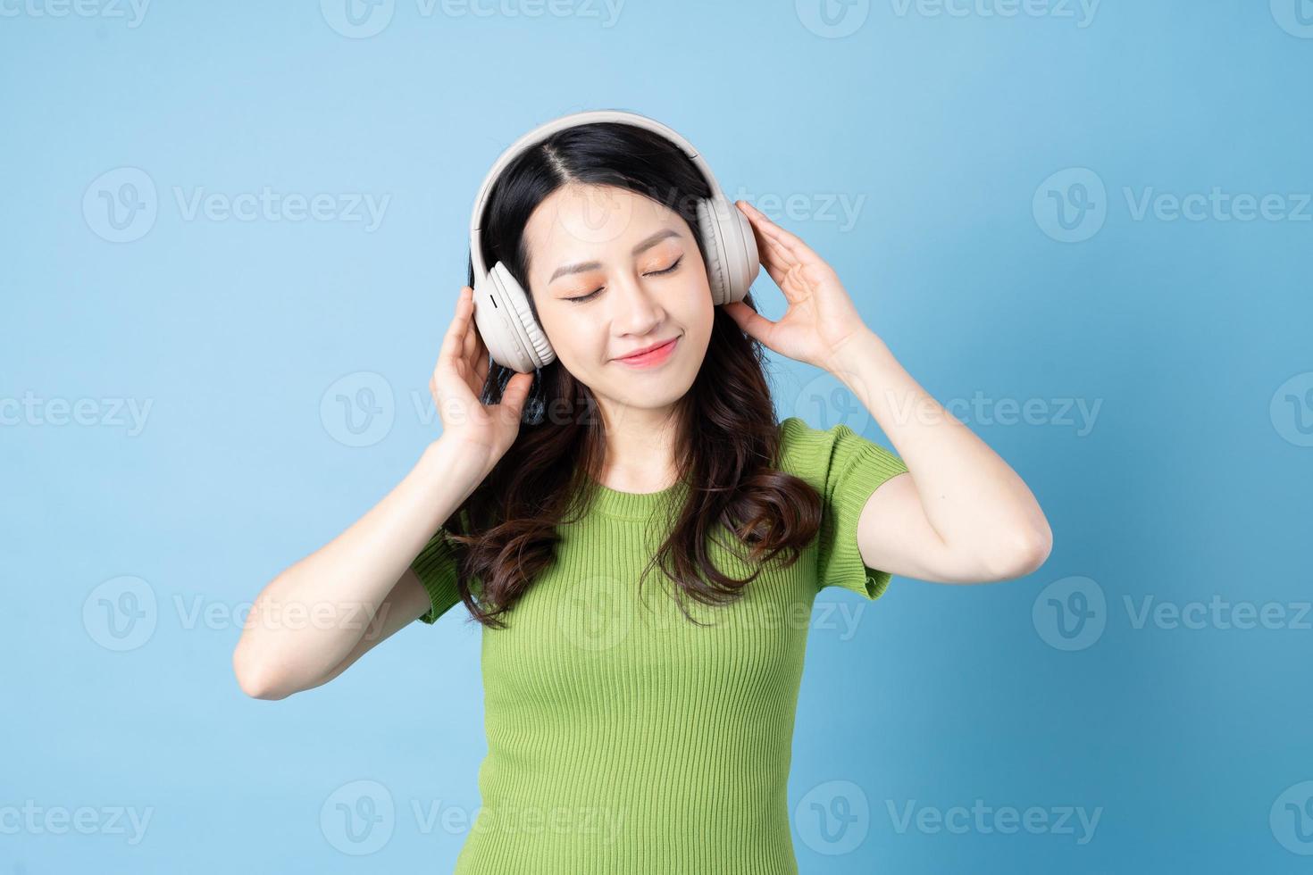 Retrato de niña asiática saltamontes está escuchando música, aislado sobre fondo azul. foto