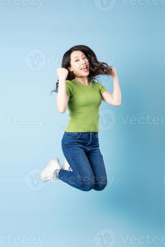 Portrait of beautiful young asian girl jumping up, isolated on blue background photo