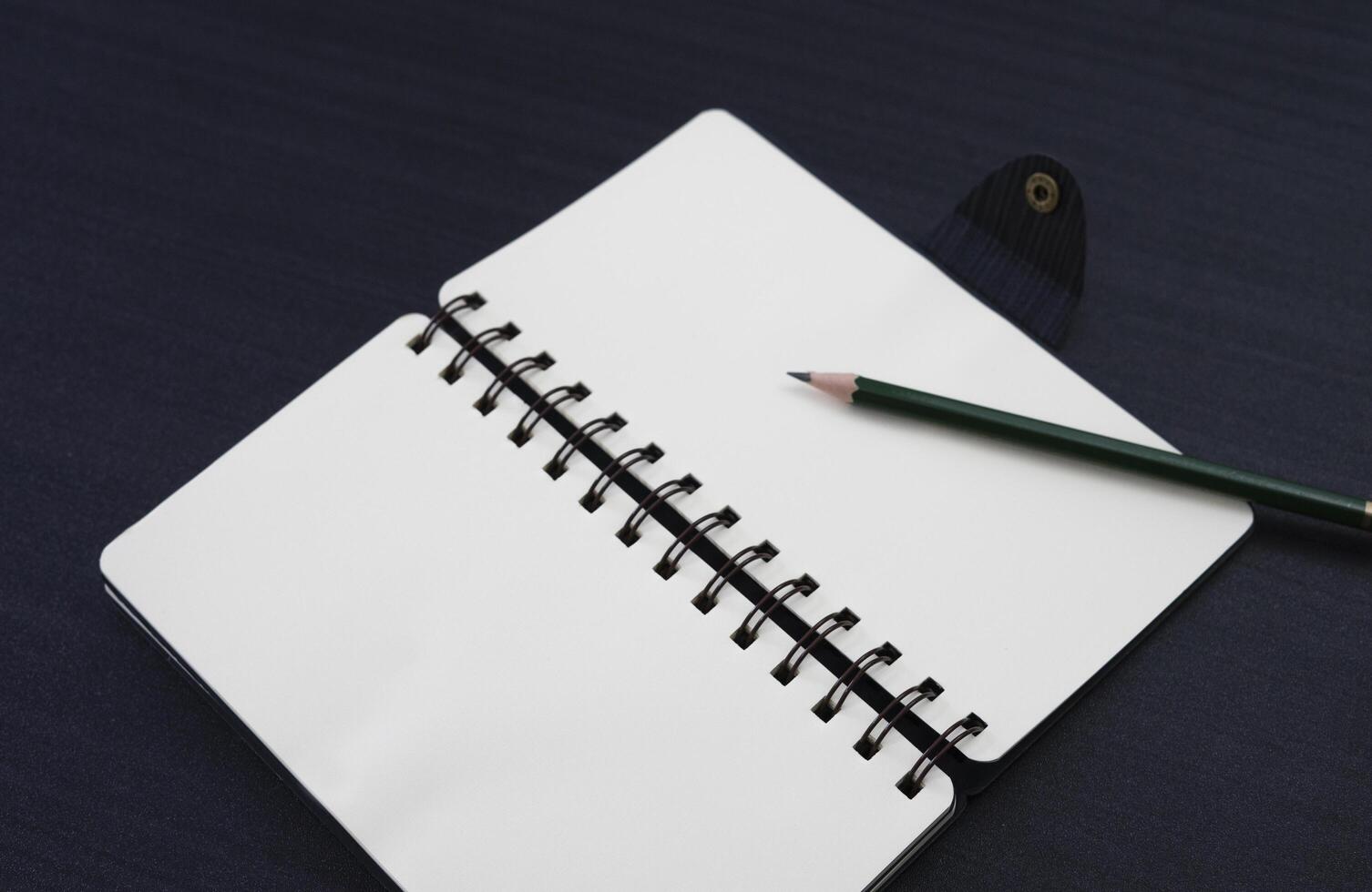 black desk with notebook and pencil on top of it. a notebook mockup on desk as a workspace layout. office object isolated on black background. photo