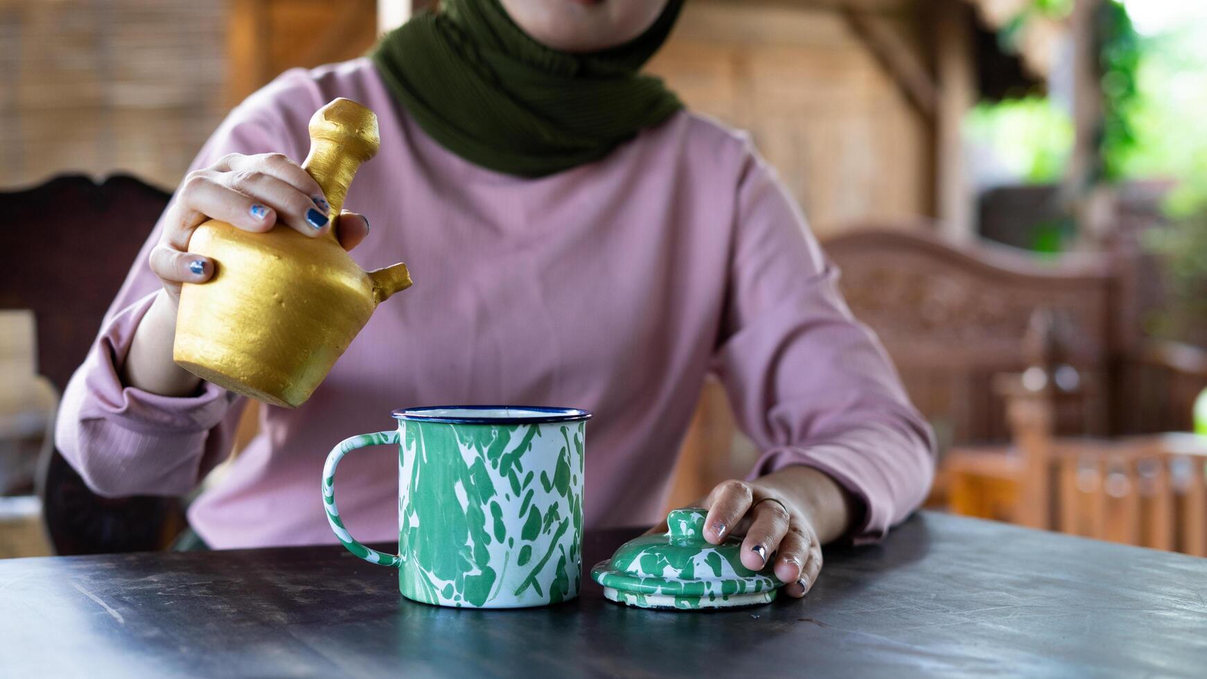 a lady pours a drink on her ethnic cup at a traditional vibes restaurant. summer vibes in Indonesia. photo