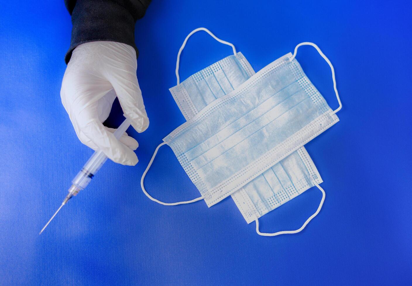 The hand holding a syringe, and there are two medical masks on a blue background. the essential goods of medical care. photo