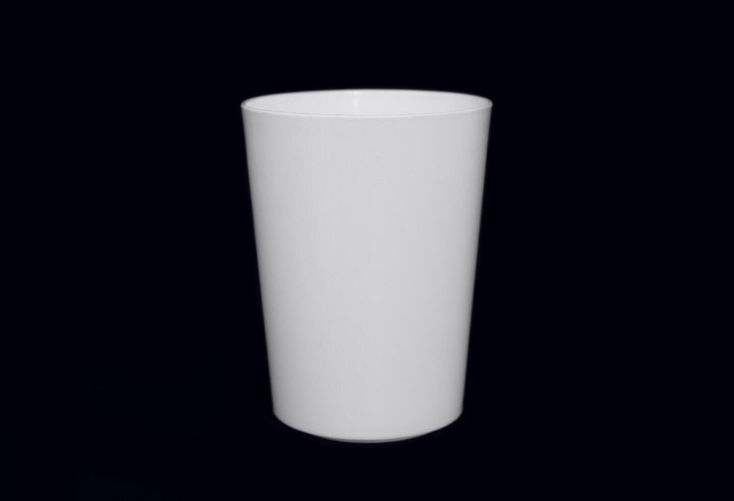 una taza de pie desde el punto de vista frontal. Disparo mínimo para una simple maqueta. Vaso de plástico blanco sobre fondo negro. maqueta realista para promoción. foto