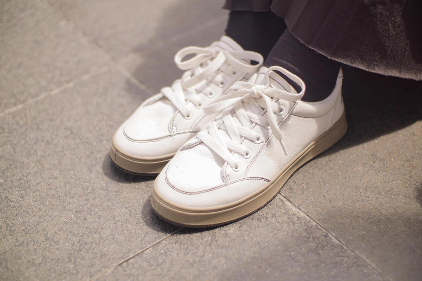 a woman wearing a black skirt is also wearing a pair of white shoes. she steps on an old tile floor. photo