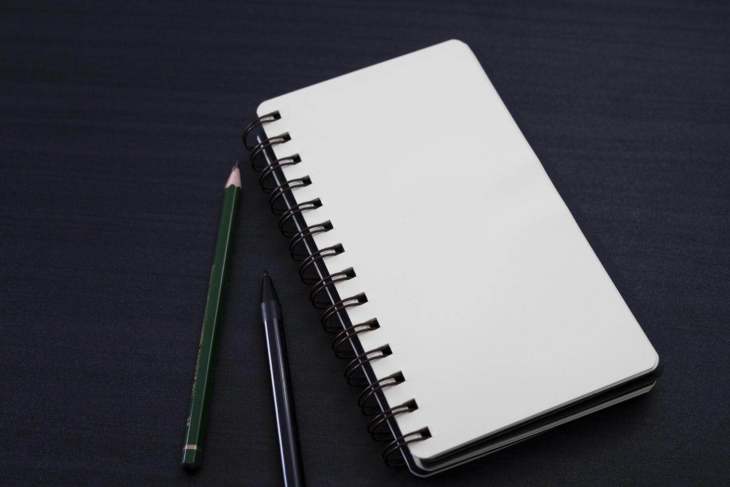 black desk with notebook and pencil on top of it. a notebook mockup on desk as a workspace layout. office object isolated on black background. photo