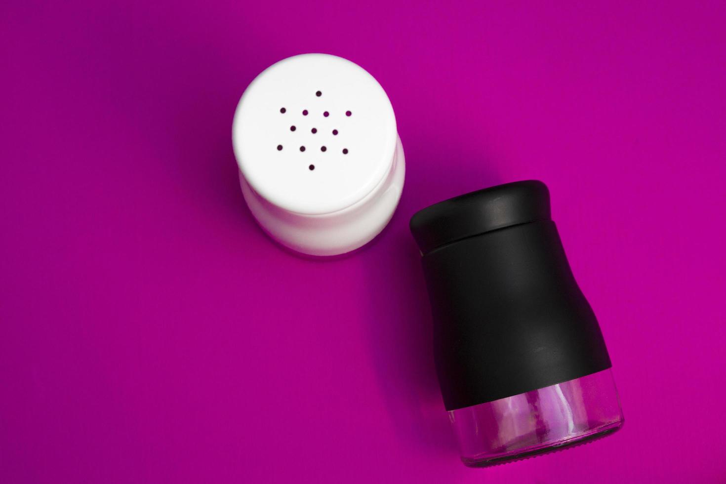 salt or pepper shaker in oblique and stand up from top view. seasoning powder container in white and black. food condiment shaker on pink background. photo