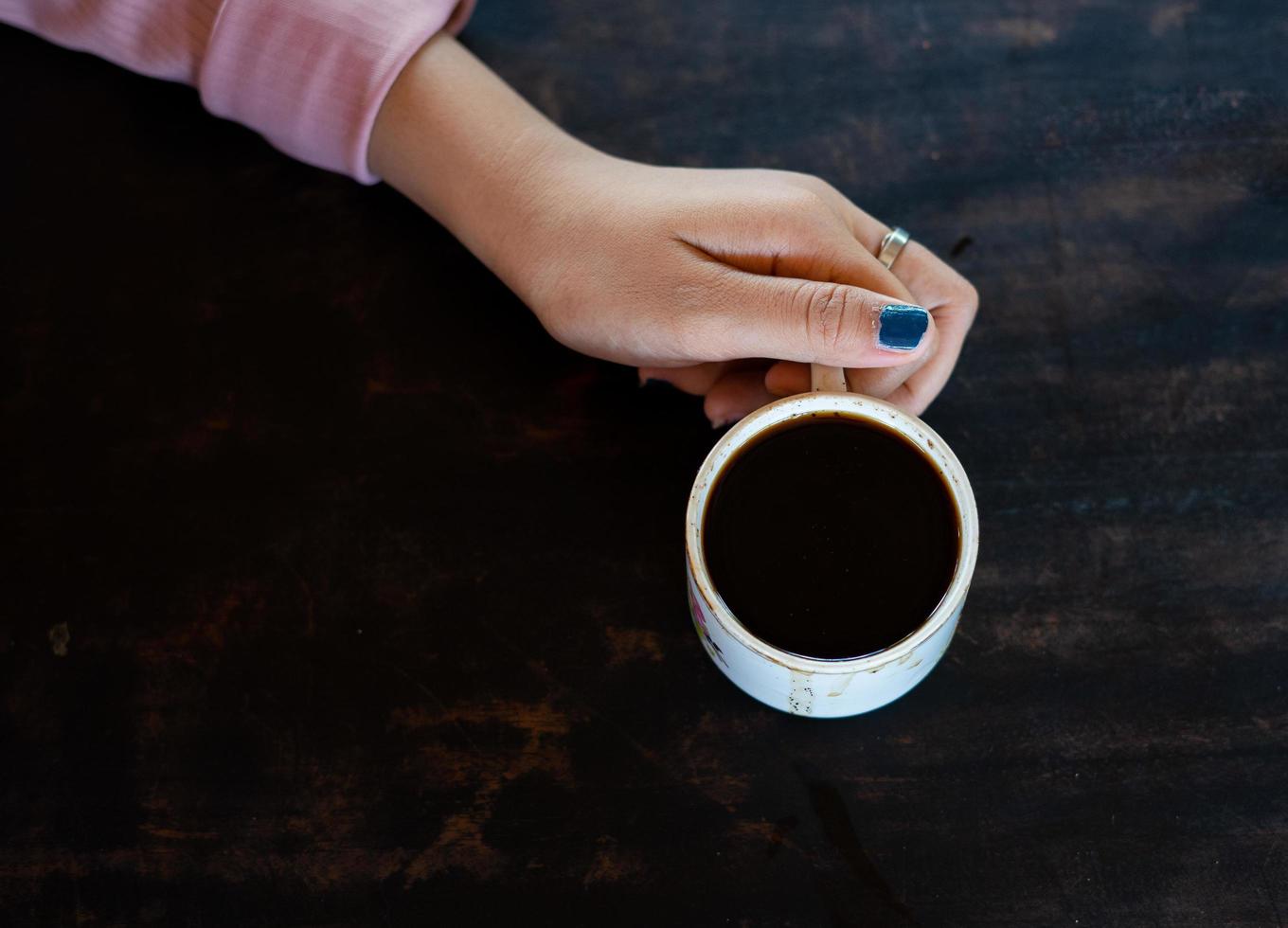 una taza de café caliente está sobre la mesa. una niña tiene una bebida sabrosa en la mano. una especie de disfrute del tiempo libre. foto