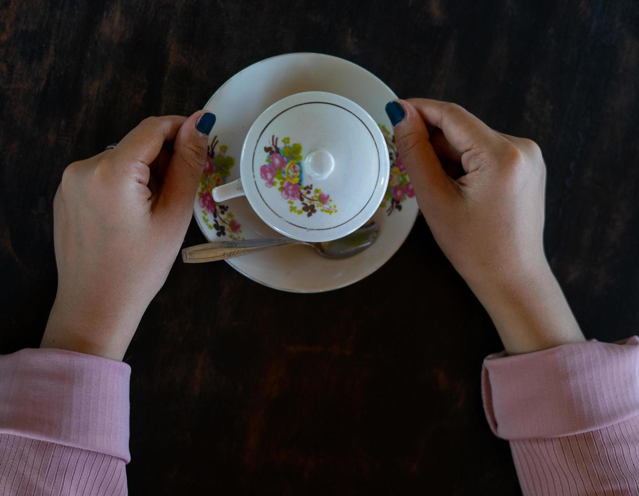 a cup of hot coffee is on the table. a girl holds a tasty beverage in her hand. a kind of enjoying leisure time. photo