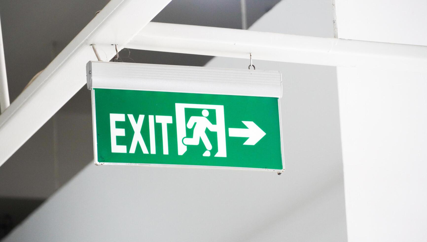 the exit route sign in green color is hanging on a white wall. the essential sign of the public places. photo